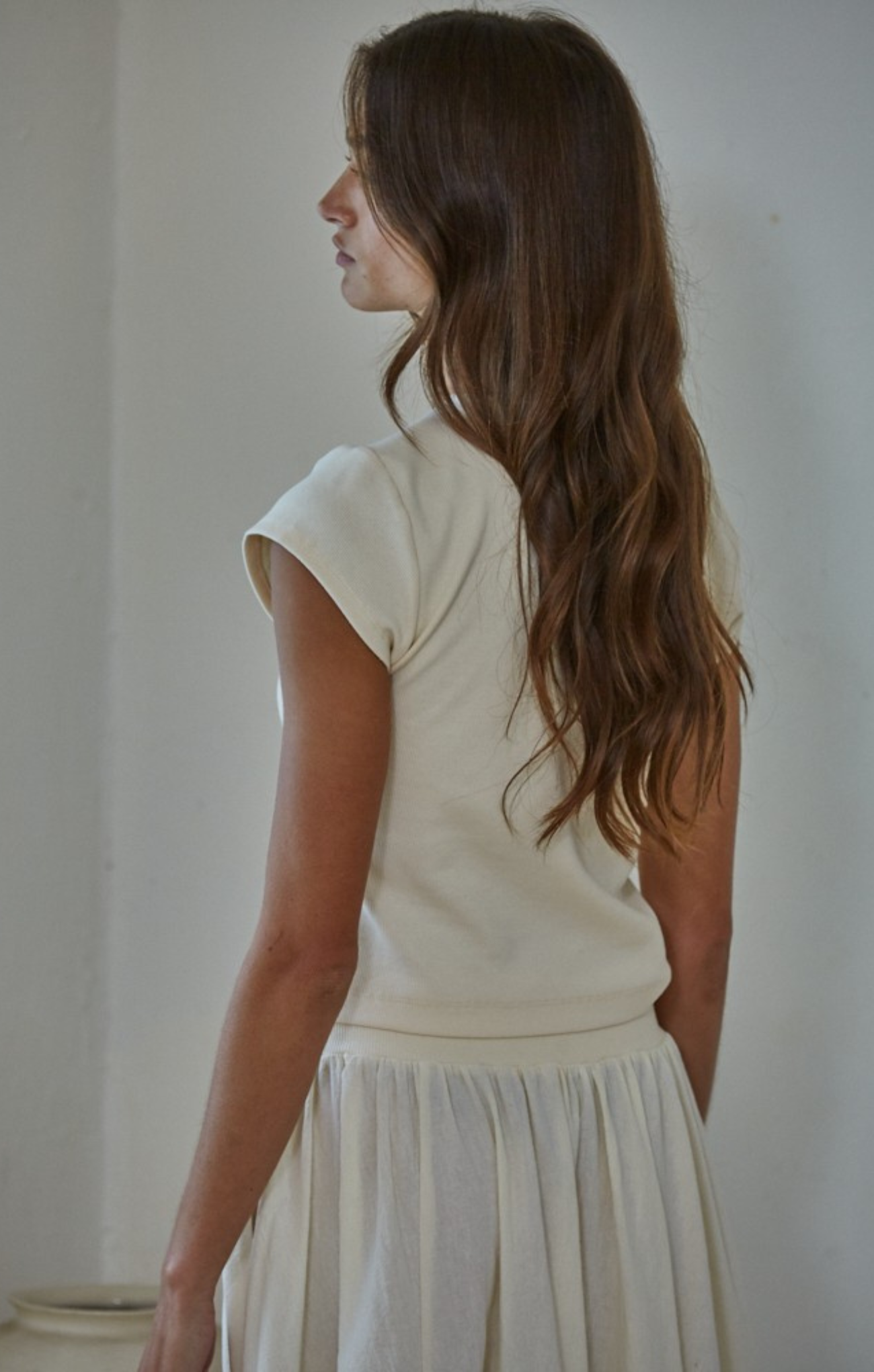 Woman wearing a light-colored top and skirt against a plain background