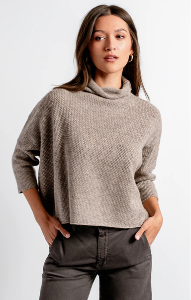 Woman wearing a gray sweater and dark pants against a white background