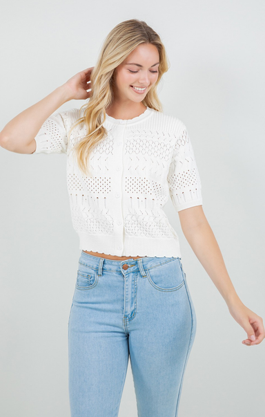 Woman wearing a white lace top and light blue jeans on a plain background