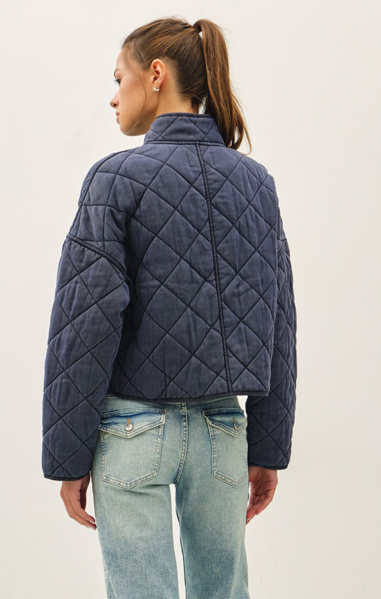 Person wearing a navy quilted jacket and light blue jeans on a plain background