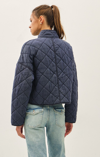 Person wearing a navy quilted jacket and light blue jeans on a plain background