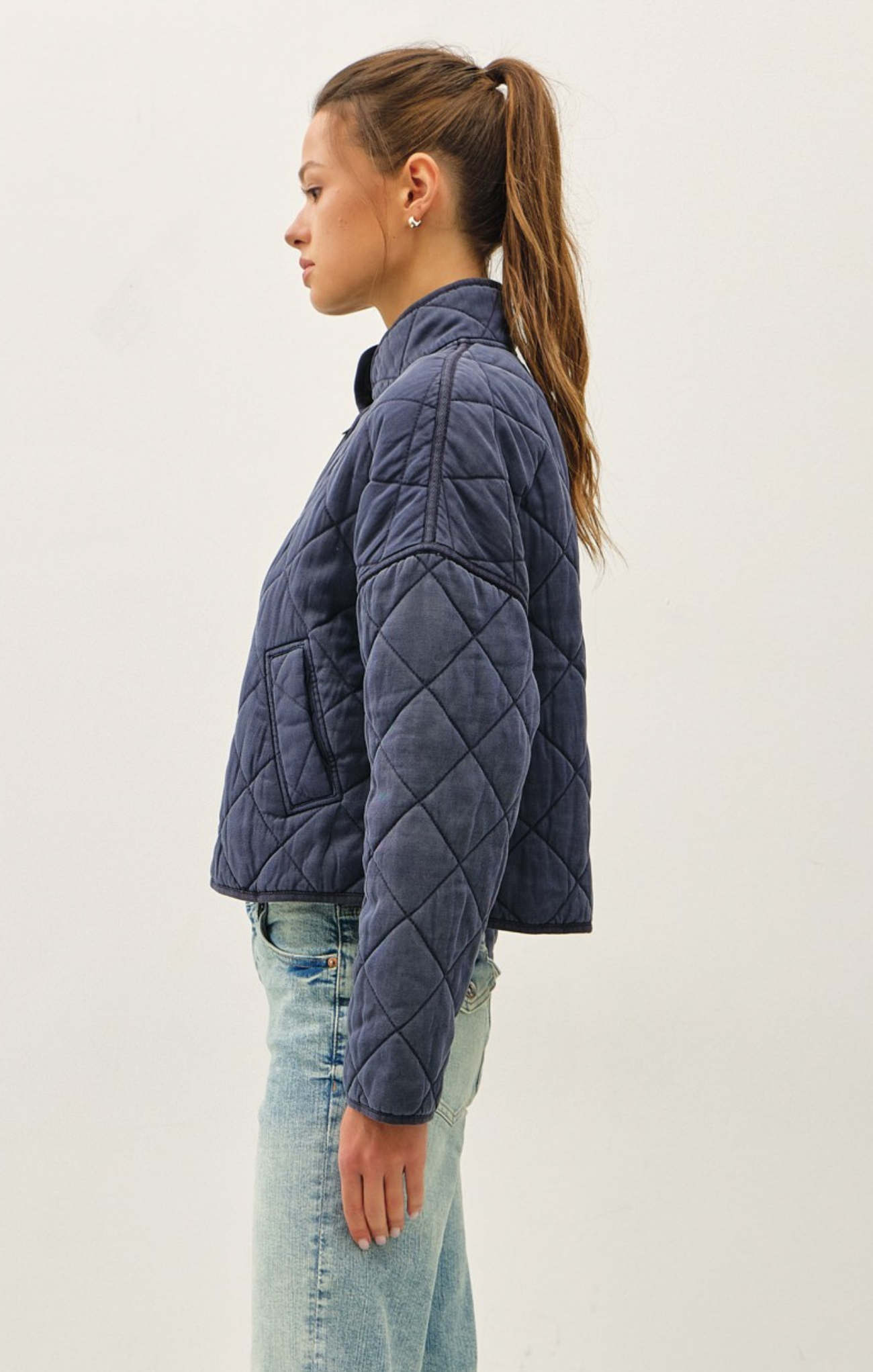 Woman wearing a blue quilted jacket and light blue jeans on a white background