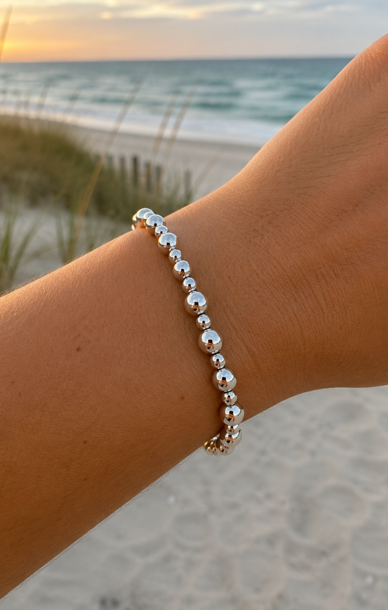 Silver beaded bracelet on a wrist with a beach background