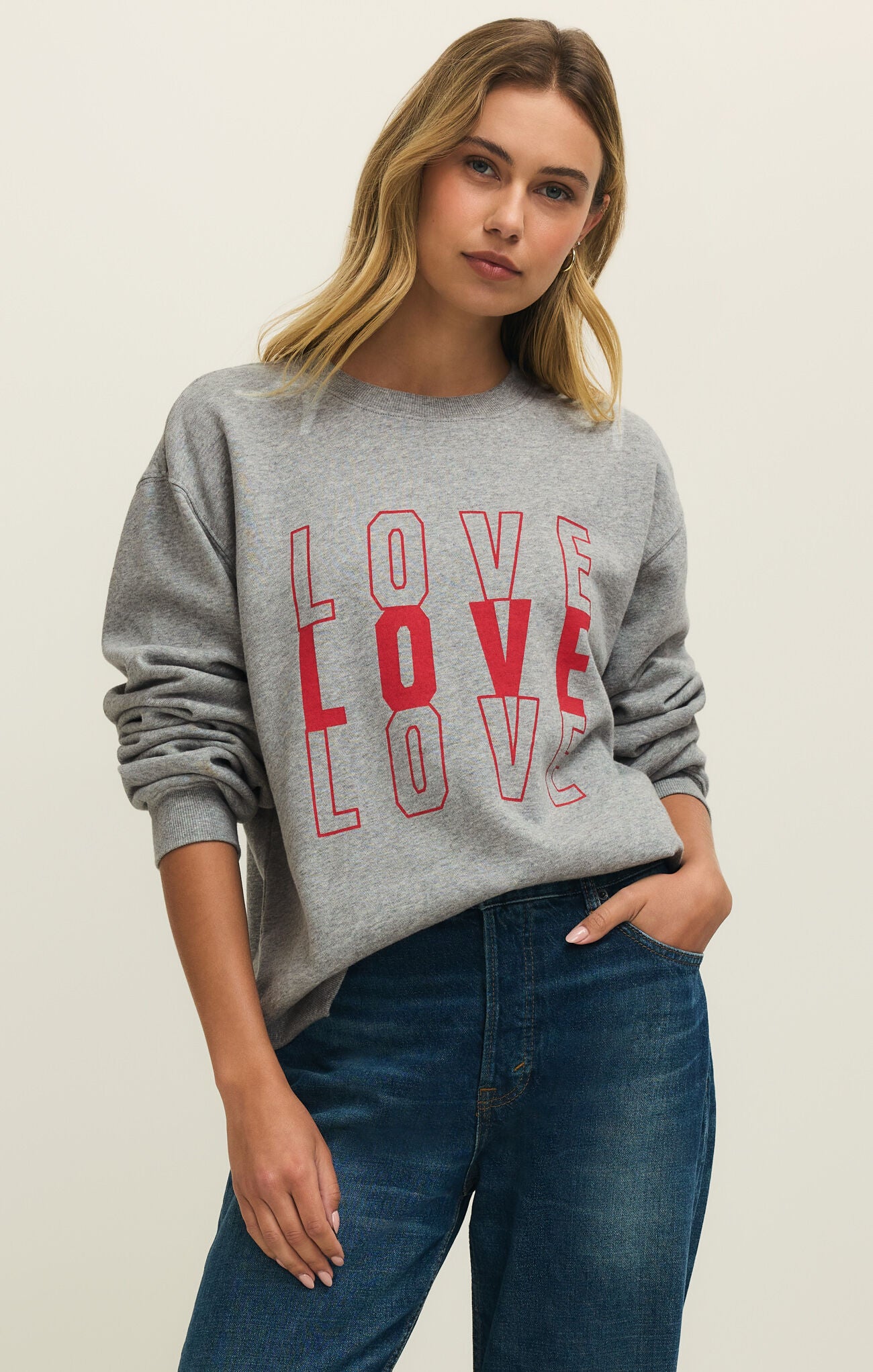 Woman wearing a gray sweatshirt with 'LOVE' printed in red, standing against a plain background.