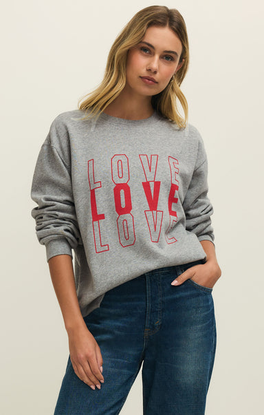 Woman wearing a gray sweatshirt with 'LOVE' printed in red, standing against a plain background.