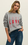 Woman wearing a gray sweatshirt with 'LOVE' printed in red, standing against a plain background.