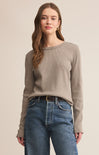 Woman wearing a beige sweater and blue jeans on a beige background