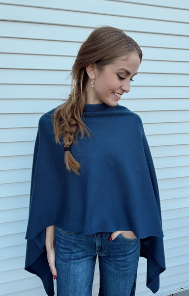 Woman wearing a blue poncho standing against a light blue wall.