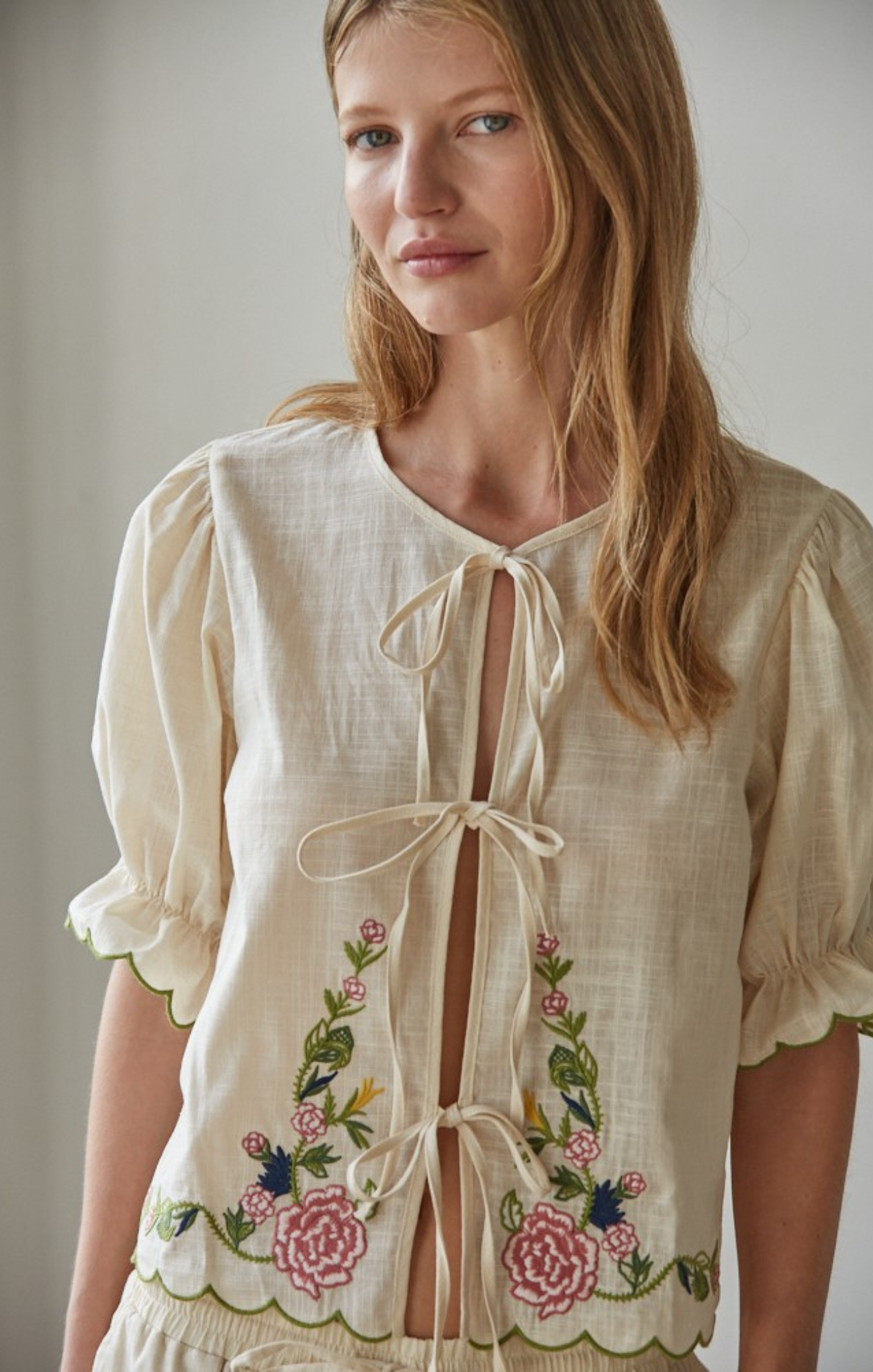 Woman wearing a cream-colored blouse with floral embroidery against a plain background