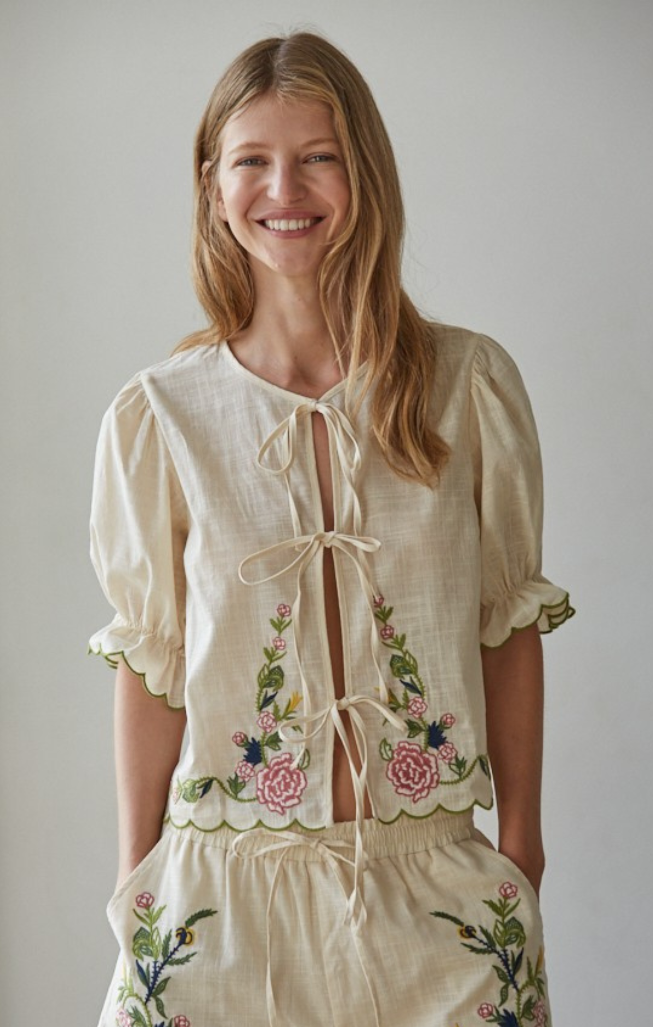 Woman wearing a cream-colored embroidered outfit against a plain background