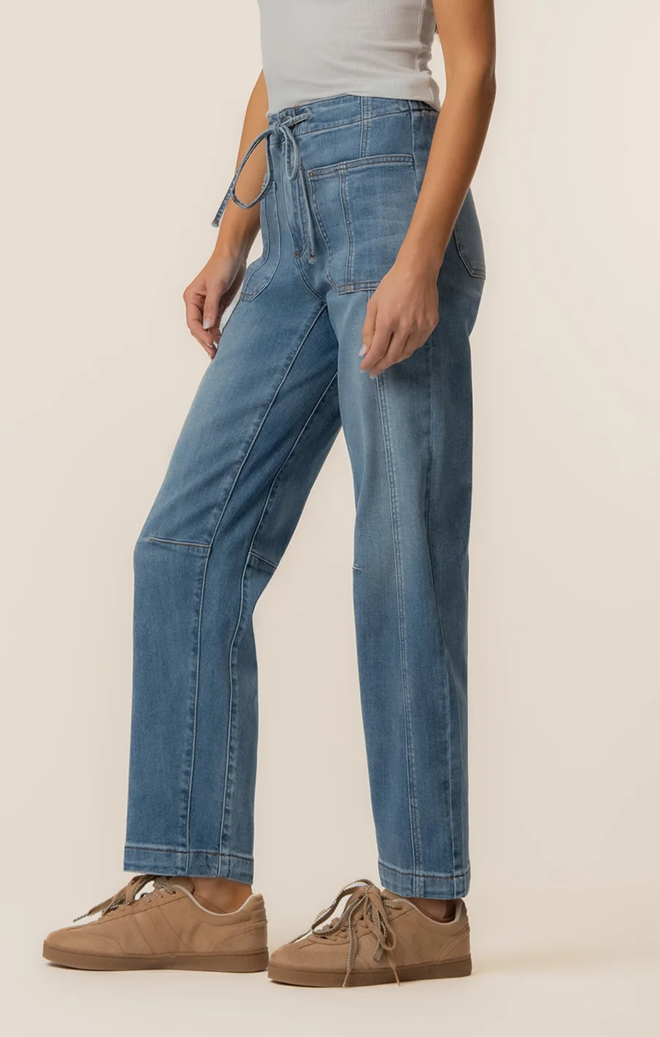 Person wearing blue jeans and brown shoes on a plain background
