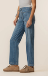 Person wearing blue jeans and brown shoes on a plain background