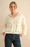 Woman wearing a cream-colored cardigan with decorative trim on a beige background