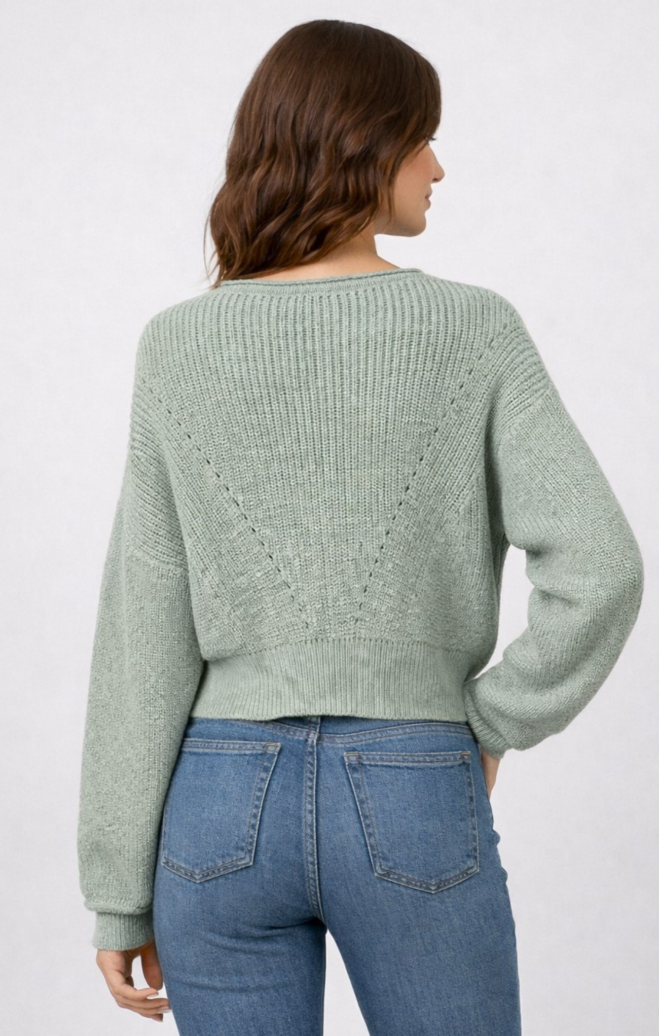 woman wearing sage green sweater with blue jeans on white background