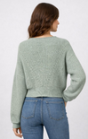 woman wearing sage green sweater with blue jeans on white background