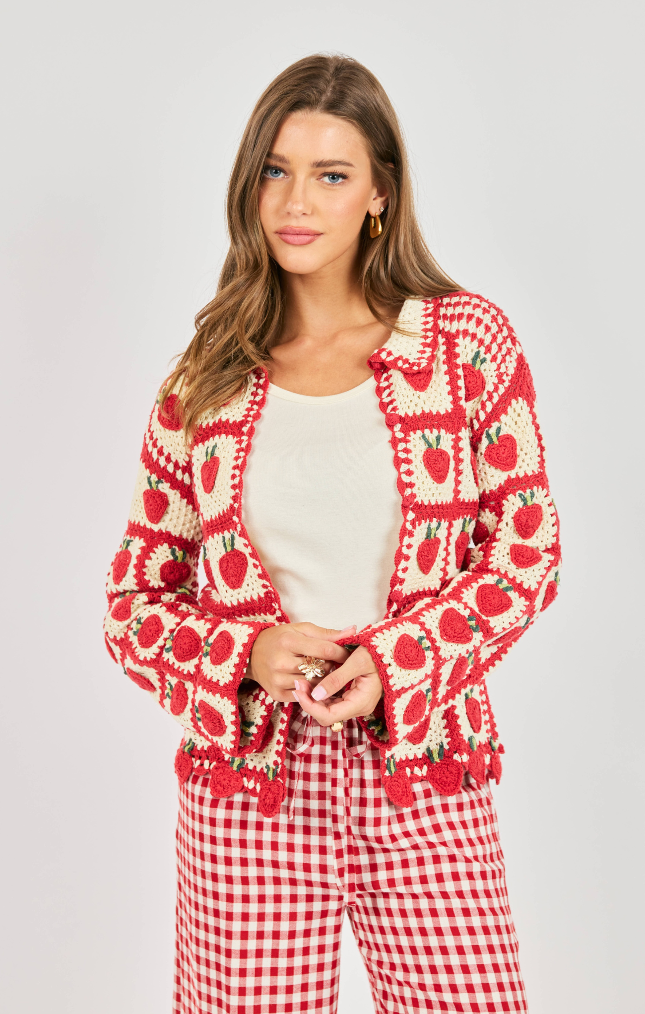 Woman wearing a red and white patterned cardigan and checkered pants on a light gray background