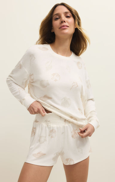Woman wearing a white long-sleeve top and shorts with floral patterns on a plain background