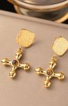 Gold cross earrings with embedded stones on a beige surface