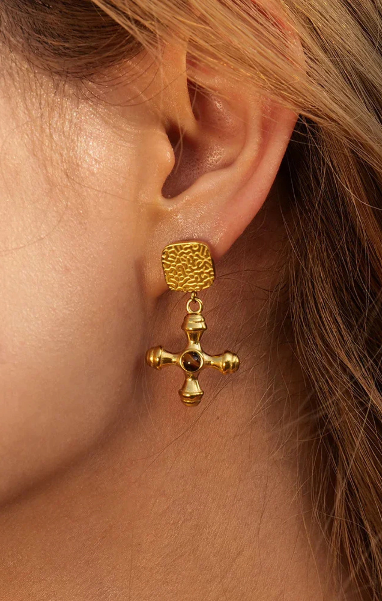 Gold cross earrings with embedded stones on a beige surface