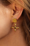Gold cross earrings with embedded stones on a beige surface
