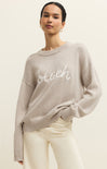 Woman wearing a beige sweater with 'beach' text on a plain background