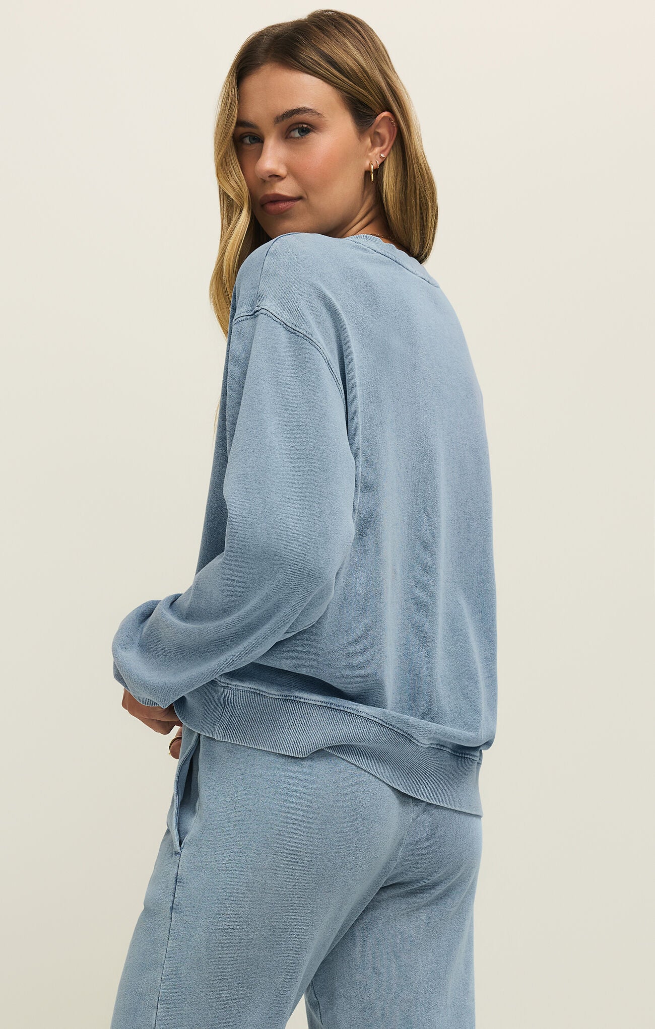 Woman wearing a light blue sweatshirt and pants on a beige background