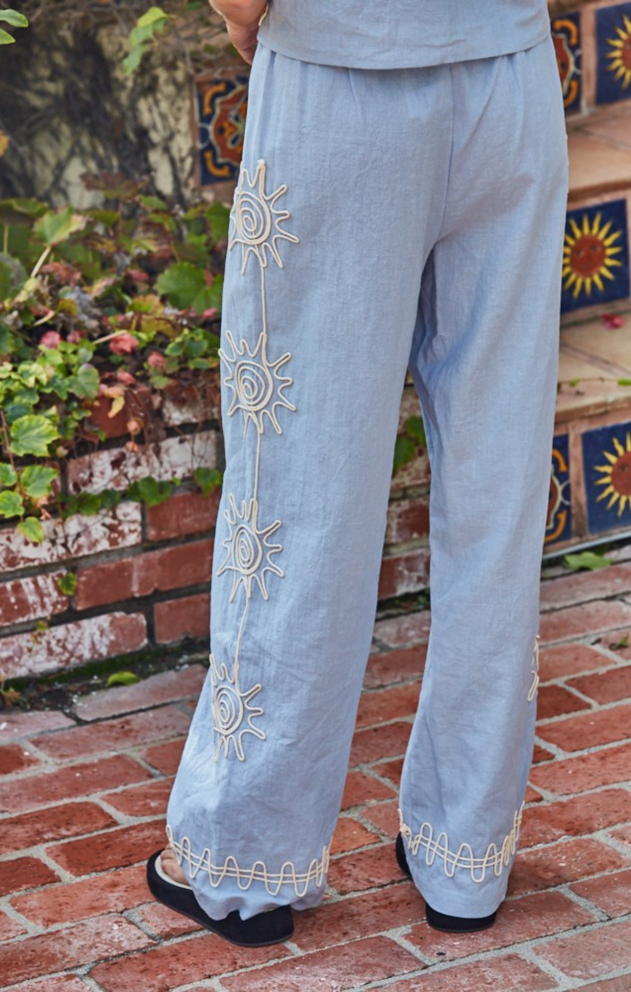 Light blue pants with sun designs on a brick ground.