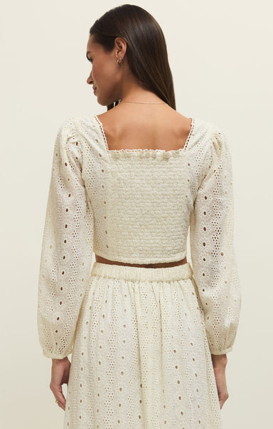 Woman wearing a cream-colored dress with long sleeves and a square neckline.