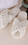 White slippers with 'Bride' and 'Groom' text in rhinestones on a light background