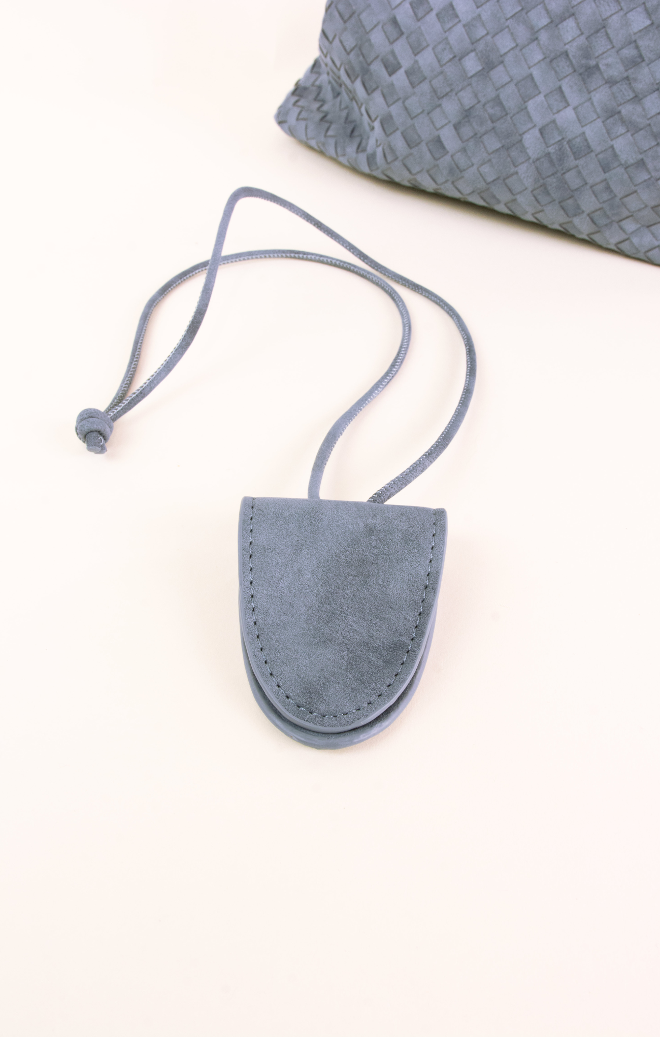 Blue suede pouch with a strap on a white surface with a textured gray pillow in the background