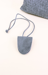 Blue suede pouch with a strap on a white surface with a textured gray pillow in the background