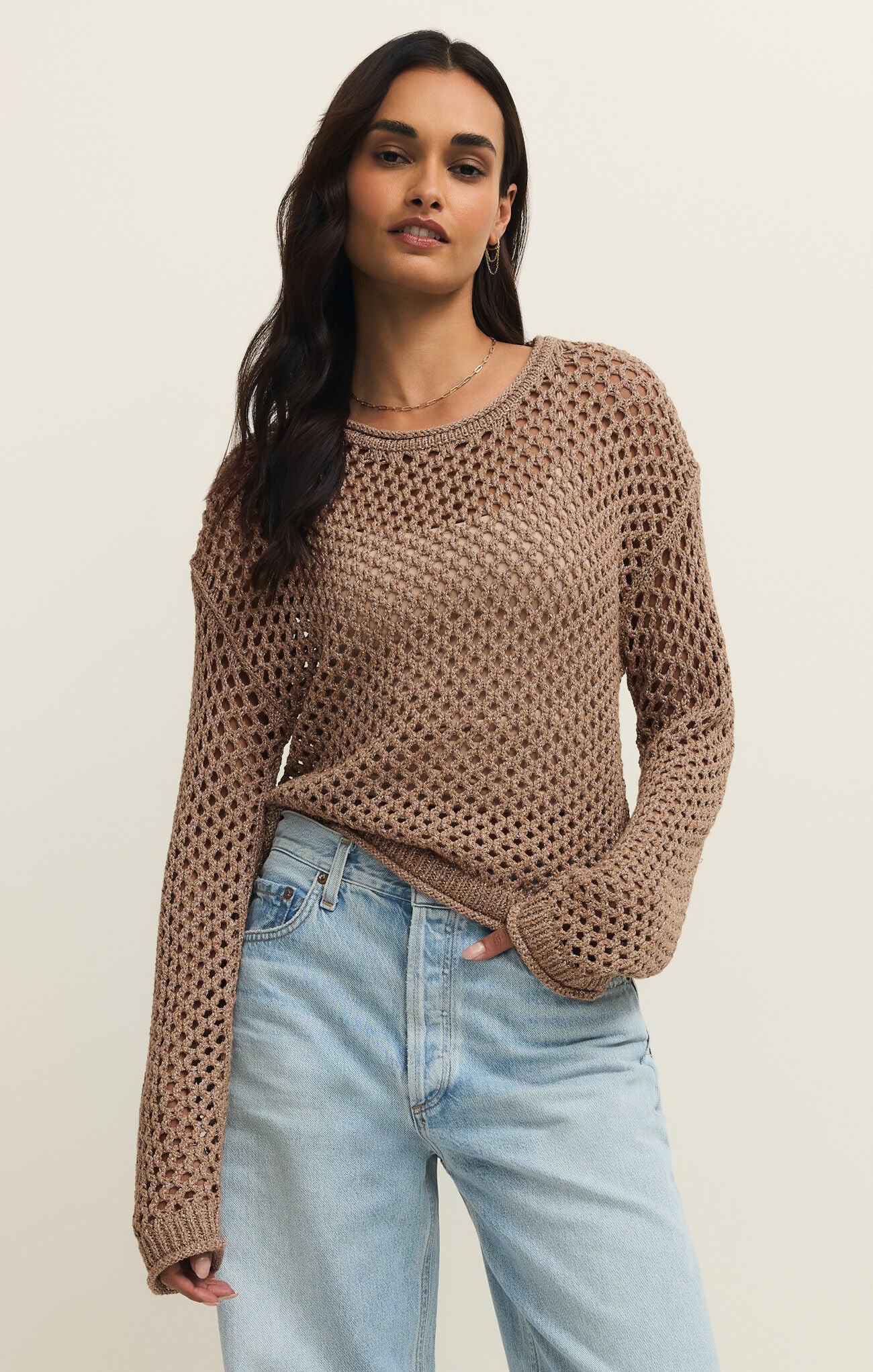 Woman wearing a brown knitted sweater and light blue jeans on a beige background