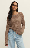 Woman wearing a brown knitted sweater and light blue jeans on a beige background