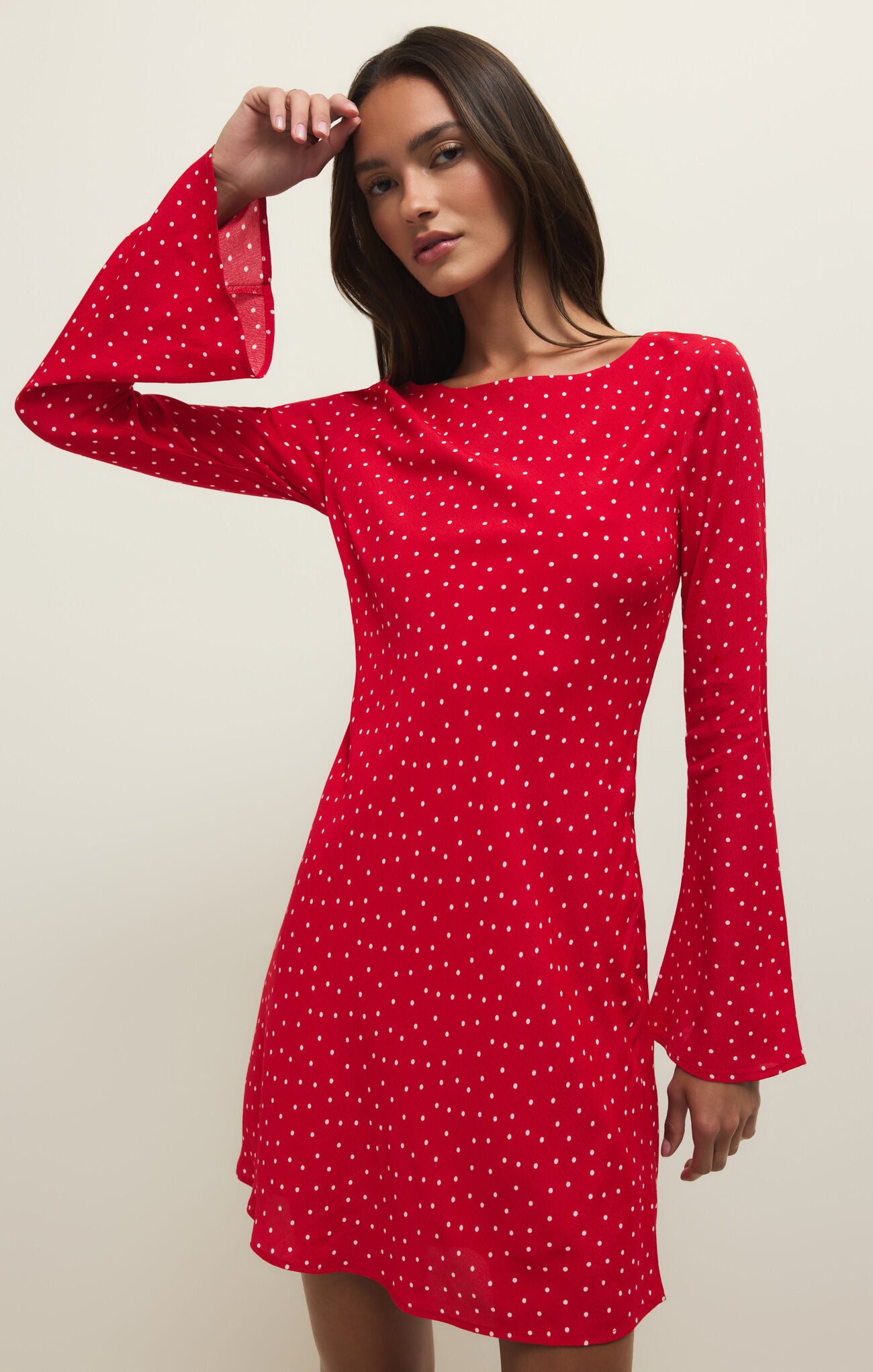 Woman wearing a red polka dot dress with bell sleeves against a beige background