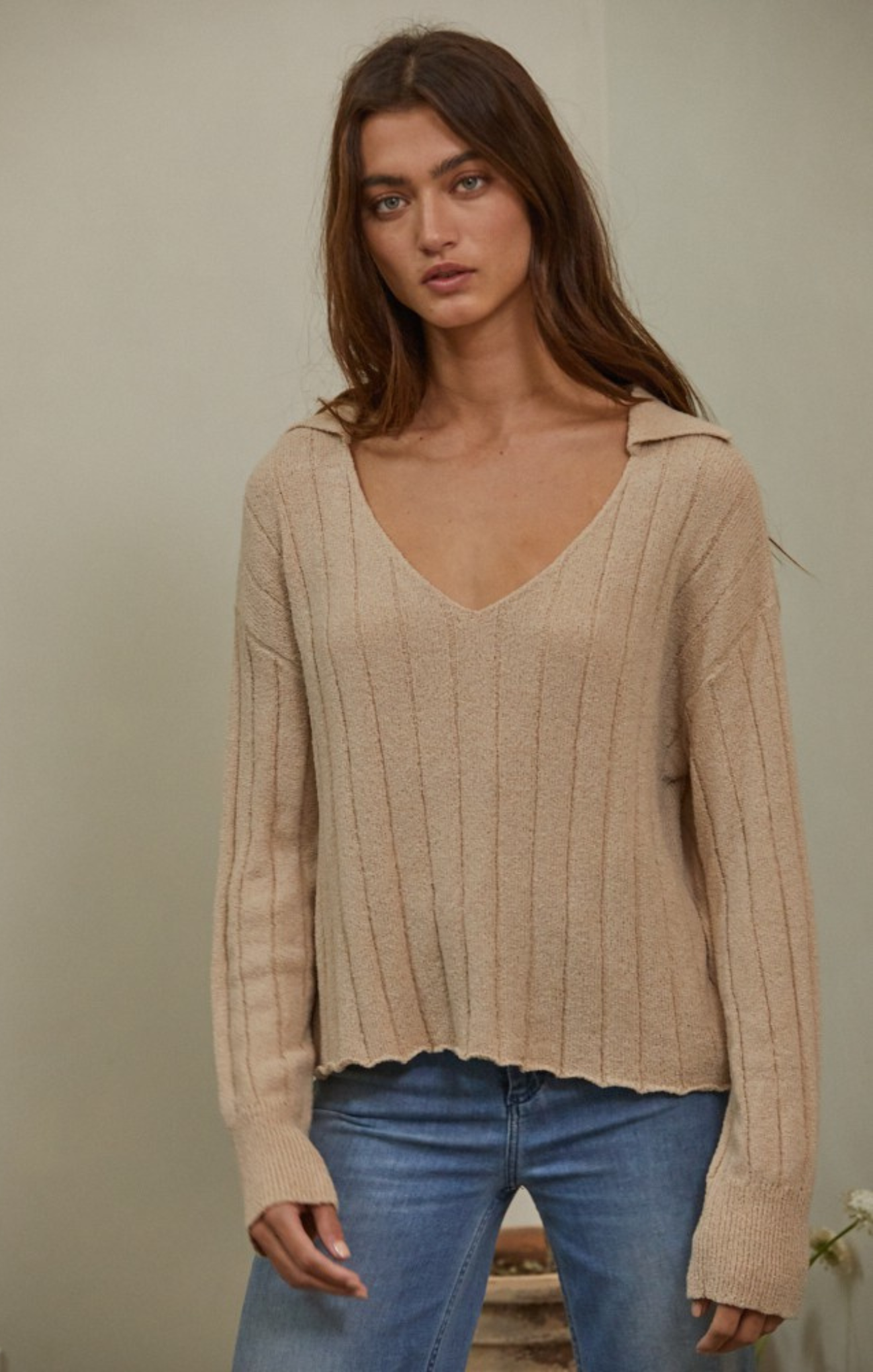 women in beige sweater and blue jeans with neutral background