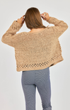 Person wearing a beige crochet sweater and blue leggings on a plain background