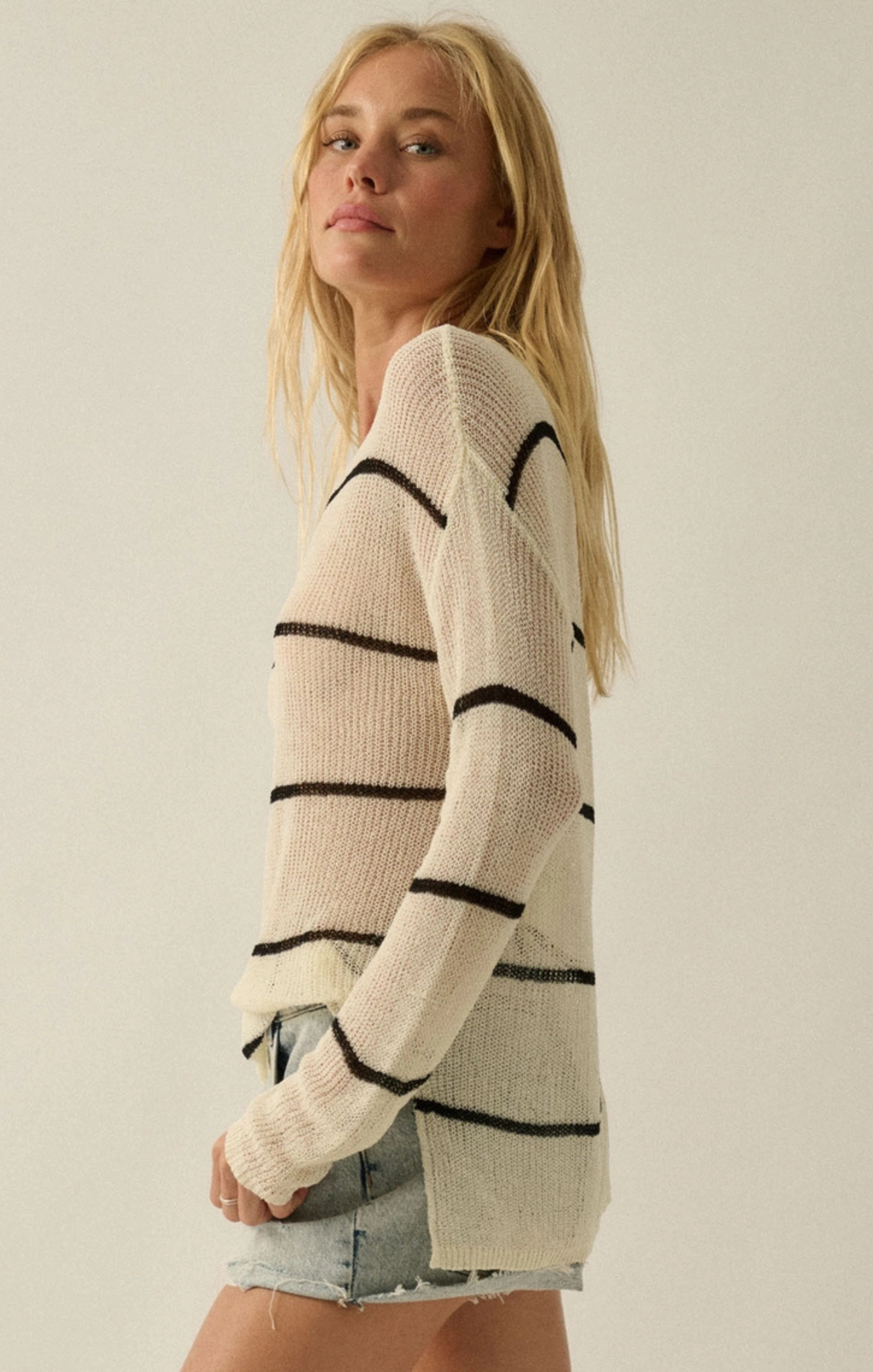 Woman wearing a cream sweater with black stripes against a plain background