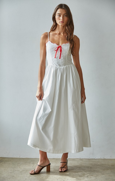 Woman wearing a white dress with a red bow detail against a plain background