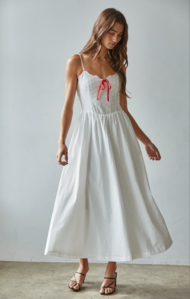 Woman wearing a white dress with red accents against a plain background