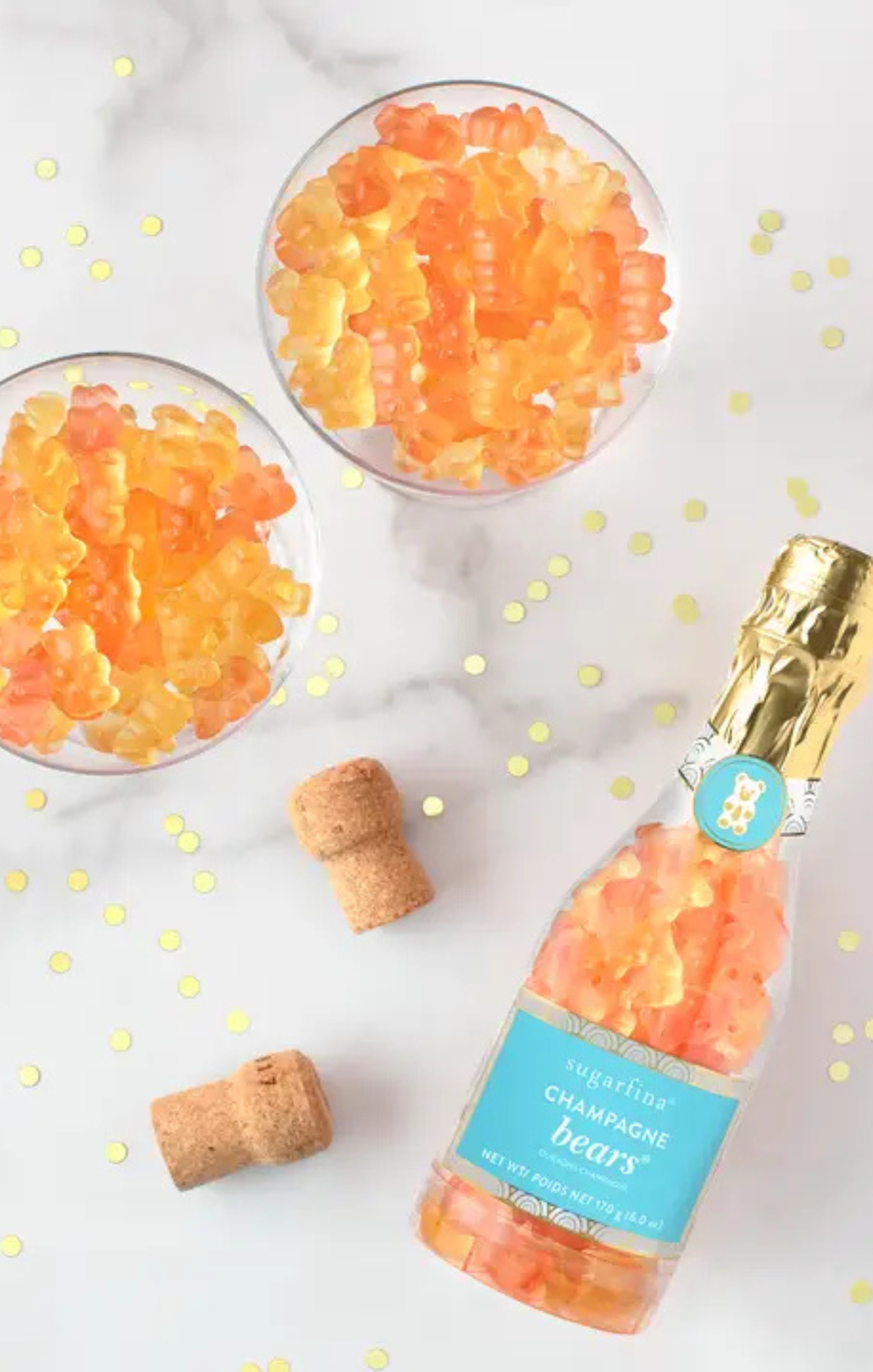 Bottle of champagne bears with two glasses filled with gummy bears on a marble surface.