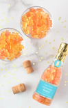 Bottle of champagne bears with two glasses filled with gummy bears on a marble surface.