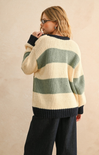 Person wearing a striped sweater with a beige and green pattern on a plain background