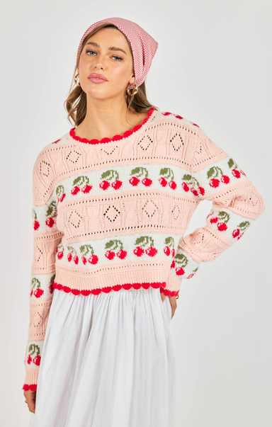 Woman wearing a pink crochet sweater with cherry patterns on a plain background