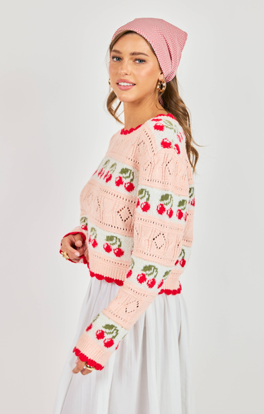Woman wearing a pink crochet cardigan with cherry pattern on a white background