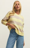 Woman wearing a yellow and brown striped sweater with blue jeans on a plain background