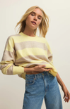 Woman wearing a yellow and beige striped sweater with blue jeans against a plain background