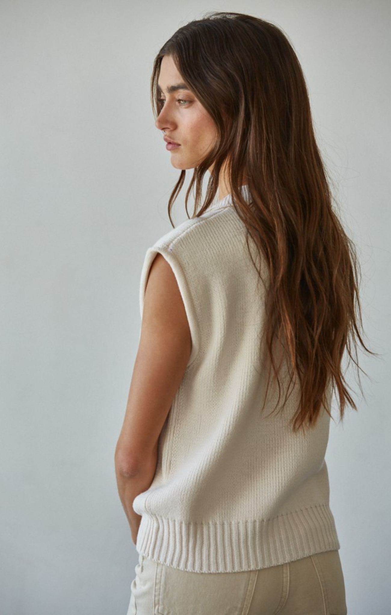 Woman wearing a beige sleeveless sweater against a plain background