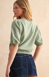 Woman wearing a green sweater and blue denim skirt against a beige background