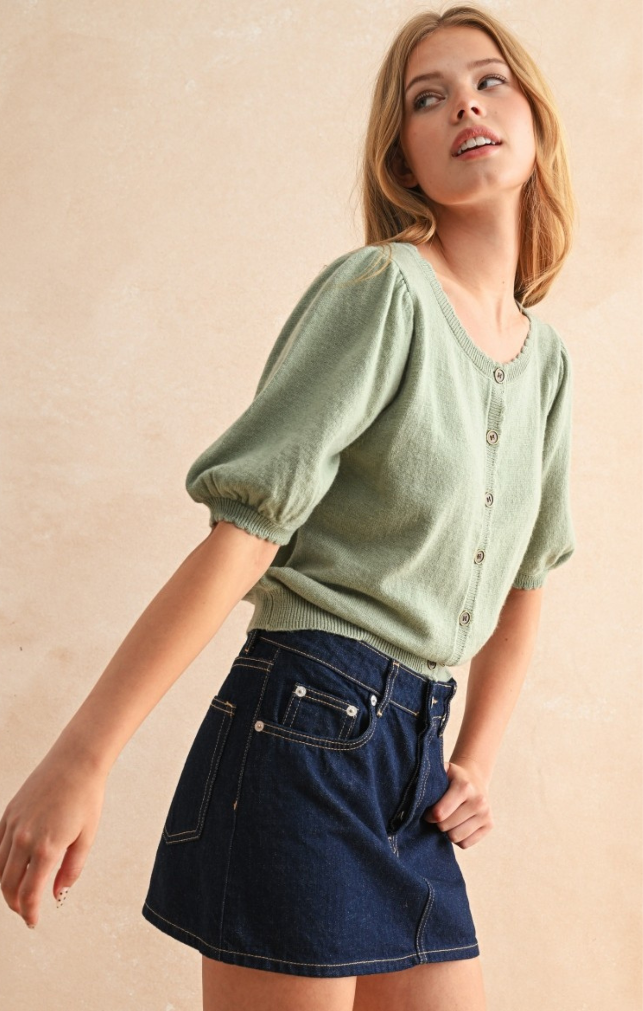 Woman wearing a green top and denim skirt against a beige background