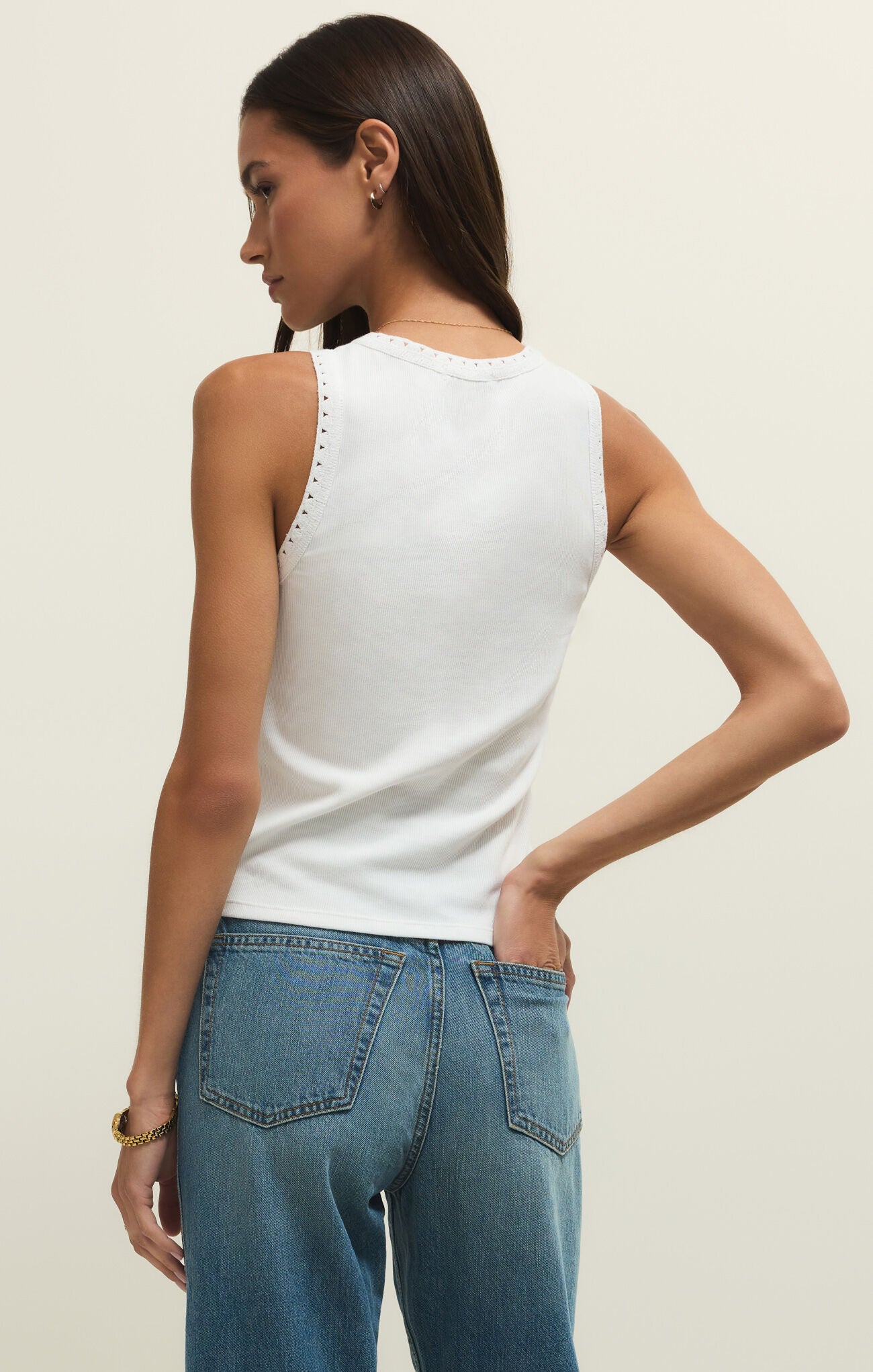 Woman wearing a white sleeveless top and blue jeans on a plain background